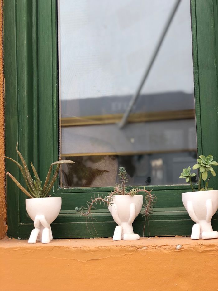 A rustic windowsill in Bozcaada, Turkey featuring potted succulents in vibrant white pots.