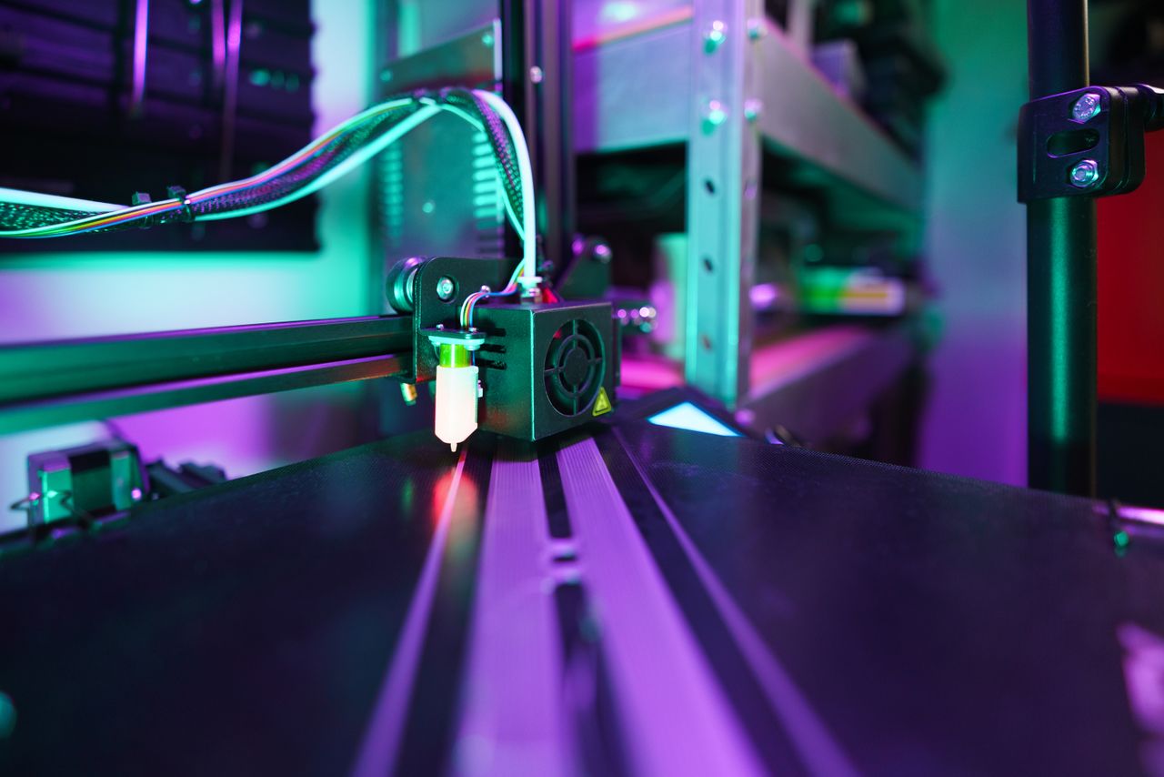 A detailed view of a 3D printer in operation with vibrant neon lighting creating a futuristic tech ambiance.
